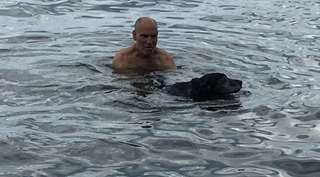 Man swimming with a black dog in the water during an outdoor outing